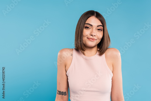 Vászonkép not knowing, smiling young woman with tattoos and nose piercing standing in tank