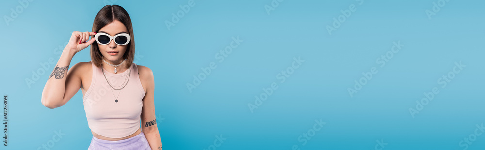 modern fashion, brunette young woman with short hair in tank top, skirt and sunglasses posing on blue background, casual attire, stylish posing, personal style, banner