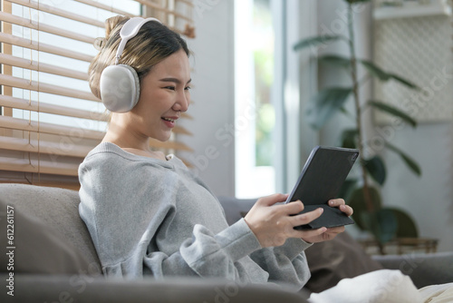 Joyful young woman wearing headphone watching movie or funny video content on digital tablet.