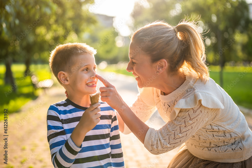 Obraz premium Portrait of happy single mother with her son in park on sunny day. Boys are eating ice cream.