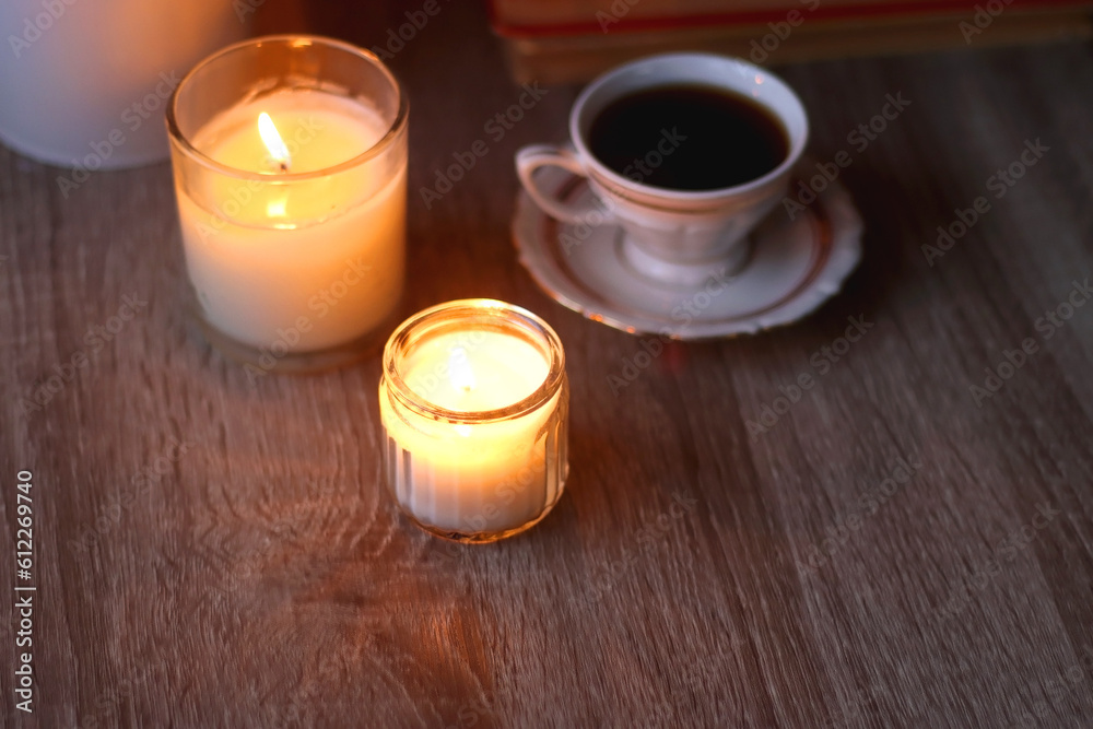Cup of tea or coffee, plate of cookies, books, e-reader, pencil and lit candles on the table. Selective focus. Cup of tea or coffee, plate of cookies, books, e-reader, pencil and lit candles on the table. Selective focus.