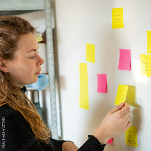 Blond young woman studying and looking at post-its at white wall