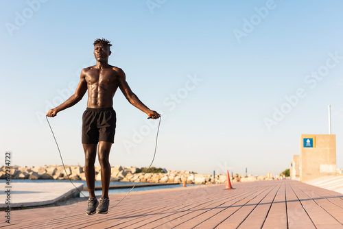 African man jumping rope on a beach. Young athlete man training outside..