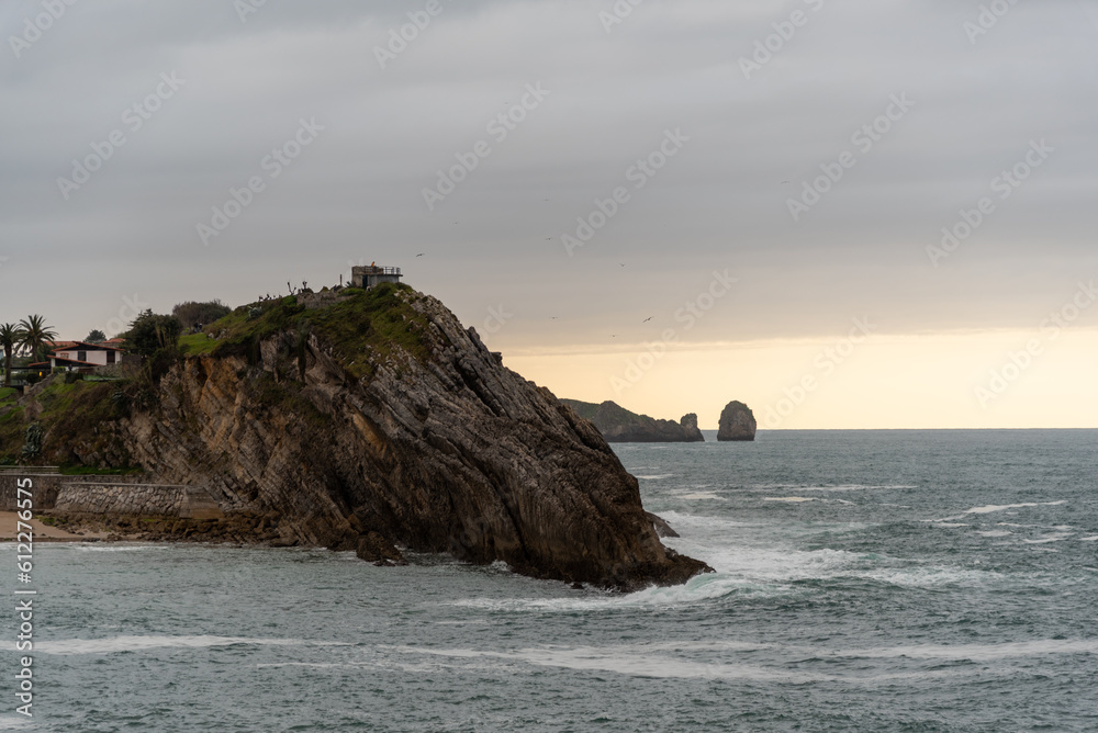 Panoramic view of the sea and cliffs surrounding the tourist town of Llanes on the coast of Asturias on a cloudy day at sunset.