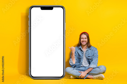 Full length photo of intelligent hipster guy dressed jeans shirt look indicating at smartphone ui menu isolated on yellow color background