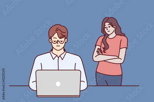 Frustrated woman near husband using laptop and suffering from internet addiction and working late into night. Concept of imbalance between internet career and family, causing resentment of loved ones