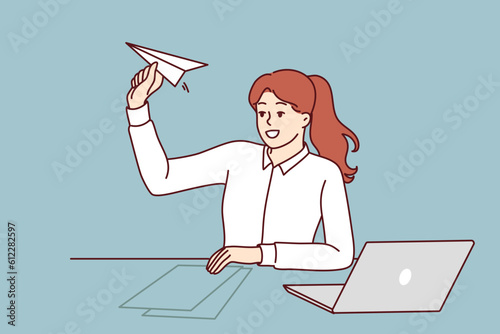 Woman office manager is distracted by launching paper plane and suffering from lack of motivation. Girl manager sits at table with laptop for metaphor of launching own successful startup