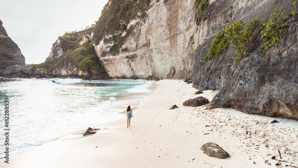 Podróżnik idący po pięknej plaży Diamond, na Indonezyjskiej wyspie Nusa Penida, plaża, skały klif oraz ocean.