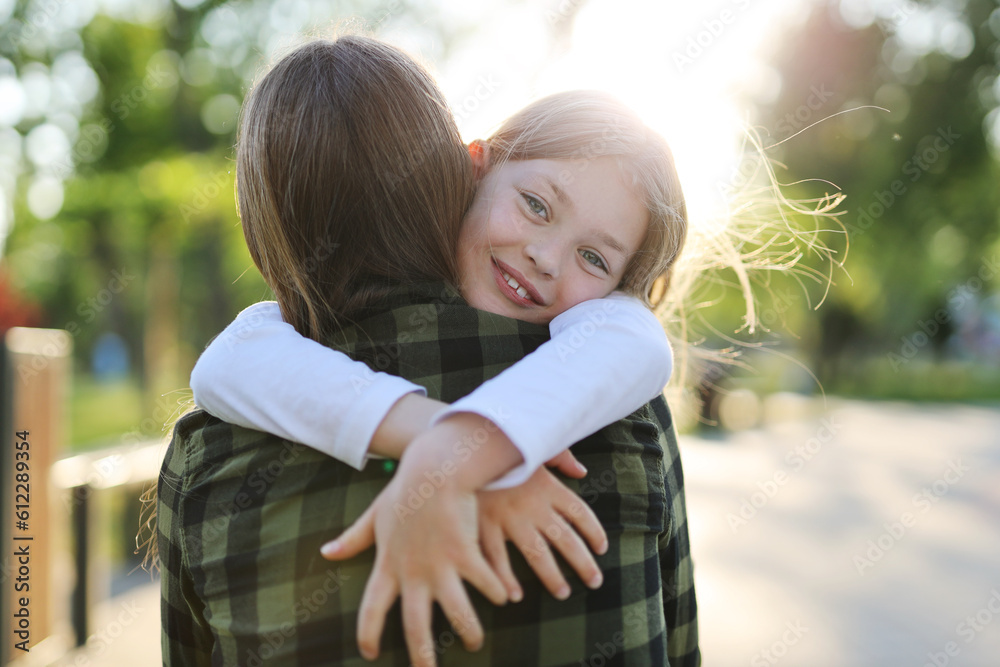 Fototapeta premium Happy child girl hugging her mother in the rays of the sunset.