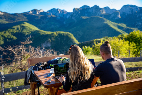 Young couple working remote as digital nomads in the sunshine on a mountain in Montenegro with a great view photo