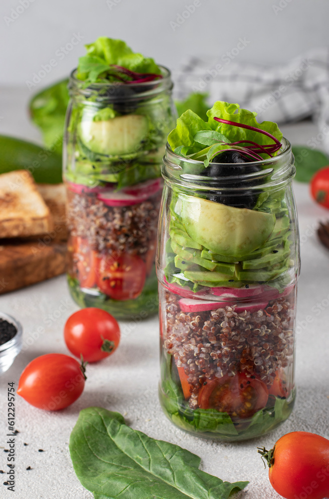 Healthy salad with quinoa, avocado, cherry tomato, radish, spinach, and olive oil in a Mason jars on gray background Healthy salad with quinoa, avocado, cherry tomato, radish, spinach, and olive oil in a Mason jars on gray background