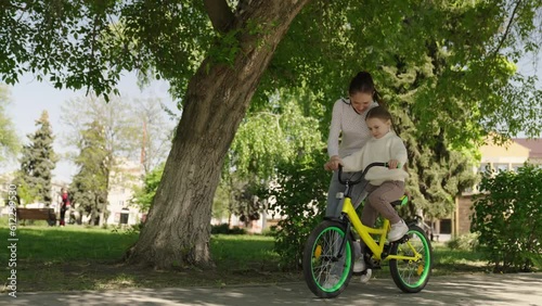 child learn ride bike. mother daughter girl drive park. happiness smile little child mom. dream family., girl spins bicycle wheel, mother teaches little smiling child ride bike, having fun with child photo