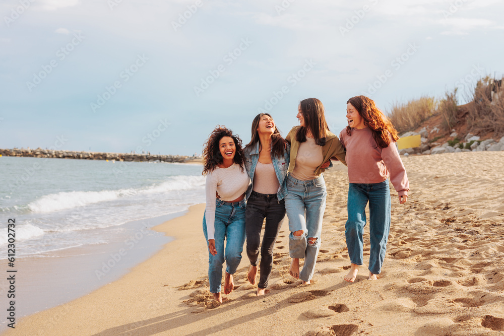 Multiracial group of four young women walking and laughing on empty beach Multiracial group of four young women walking and laughing on empty beach