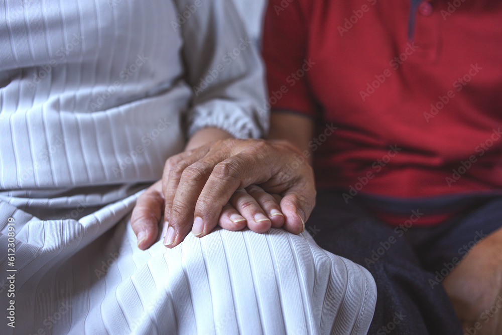 Obraz premium Cropped shot of elderly couple holding hands while sitting together at home