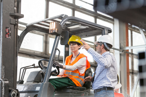 Supervisor directing worker driving forklift in factory