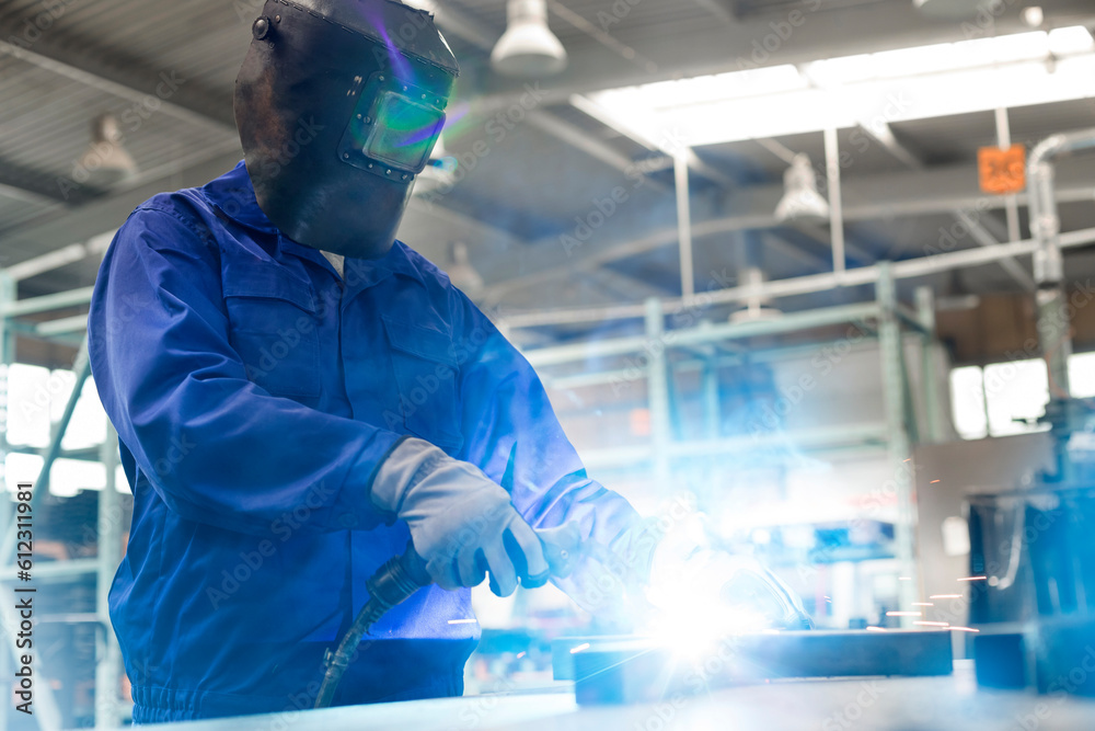 Welder in protective workwear using welding torch in steel factory