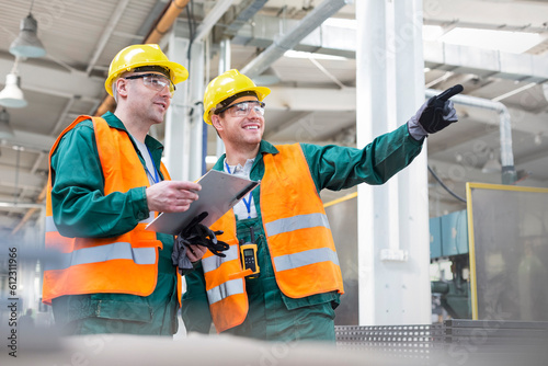Tableau sur toile Workers in protective workwear talking with clipboard in factory