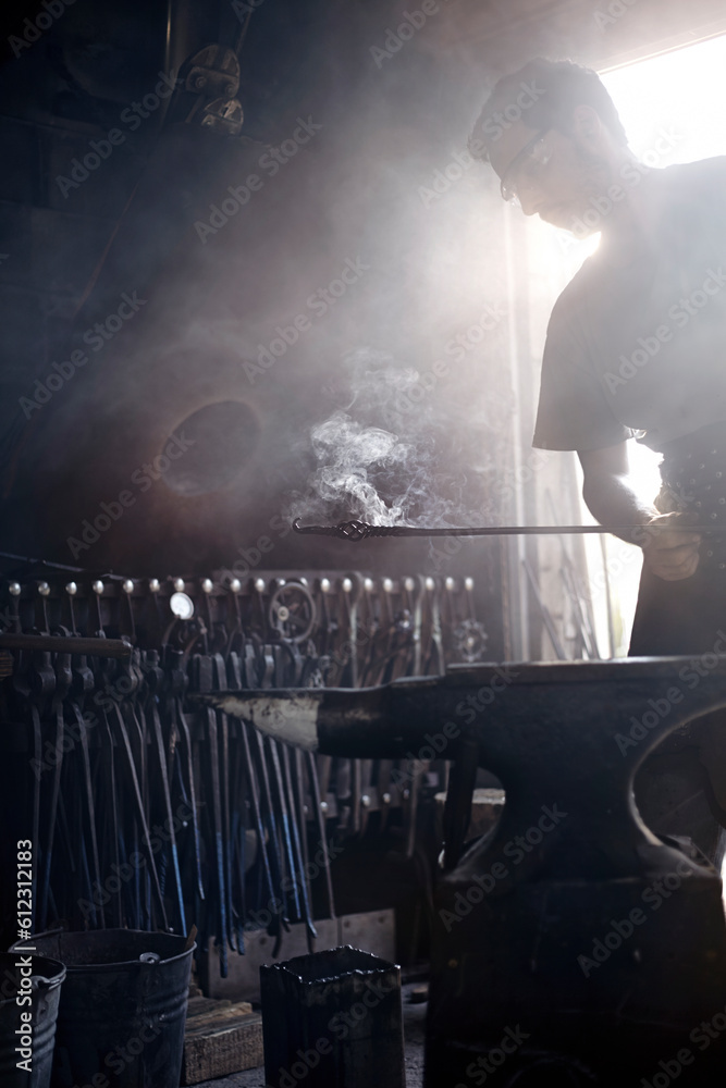 Fototapeta premium Blacksmith holding steaming wrought iron over anvil in forge