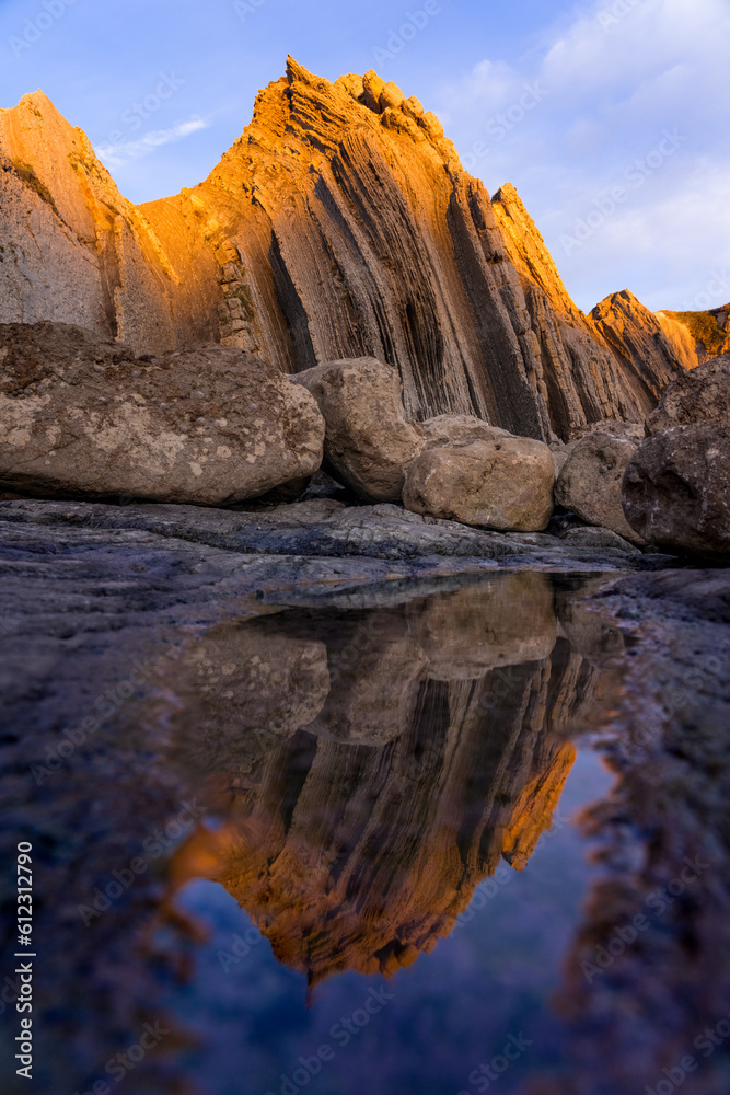 Reflection landscape of a colorful rock formations (Flysch) of the Portio beach at sunset in Cantabria, north of Spain.