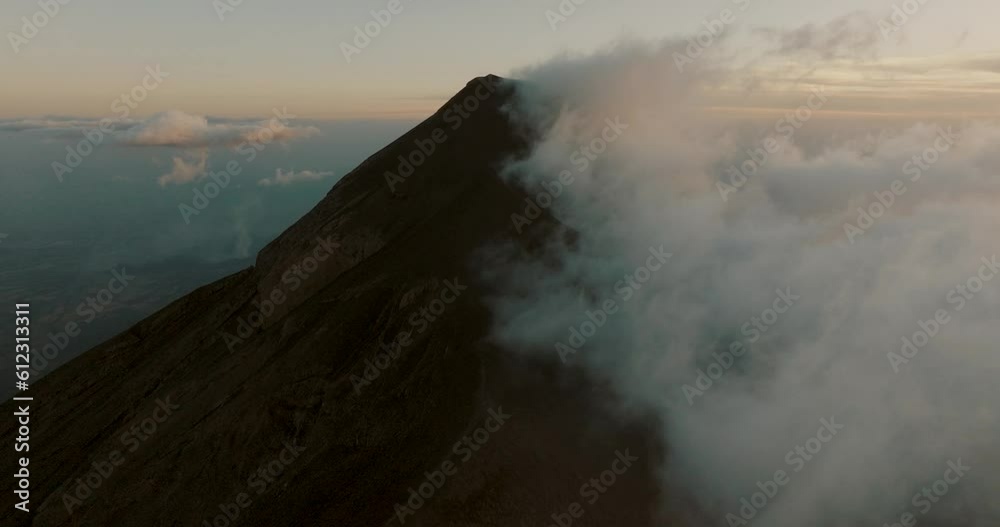 Tilt-up aerial of Fuego volcano covered by clouds during sunset in Guatemala
