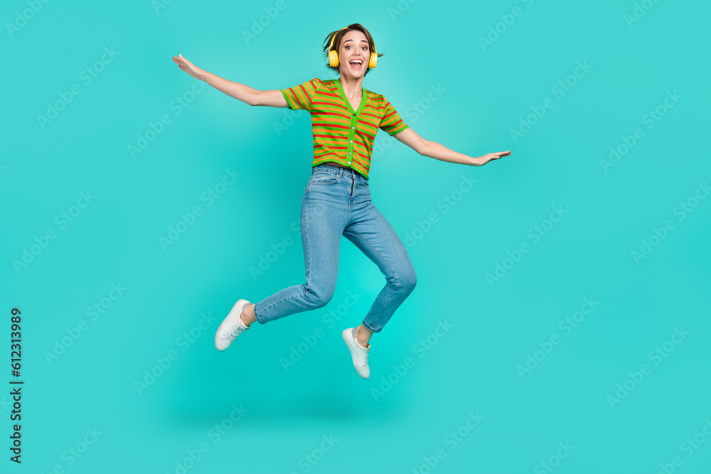 Full length photo of overjoyed person jumping enjoy listen favorite song isolated on teal color background