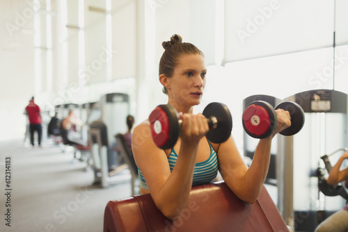 Focused woman doing dumbbell biceps curls at gym © KOTO