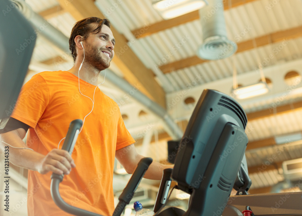 Smiling man with headphones using elliptical trainer at gym Smiling man with headphones using elliptical trainer at gym