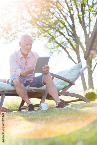 Senior man using digital tablet on lounge chair in backyard