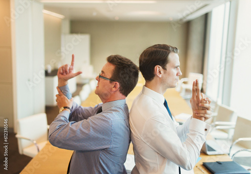 Canvas Print Playful businessmen pretending to duel back to back in conference room