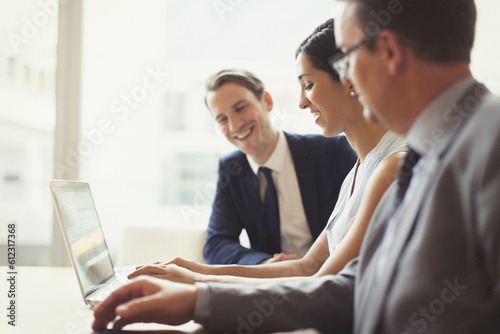 Smiling business people using laptop in conference room