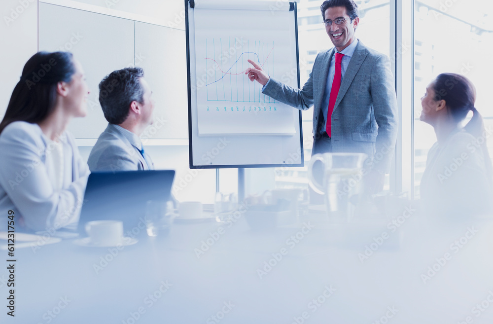 Obraz premium Smiling businessman leading meeting at flip chart in conference room