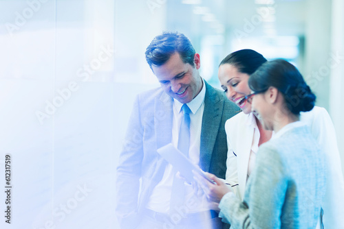 Business people with digital tablet laughing in office corridor
