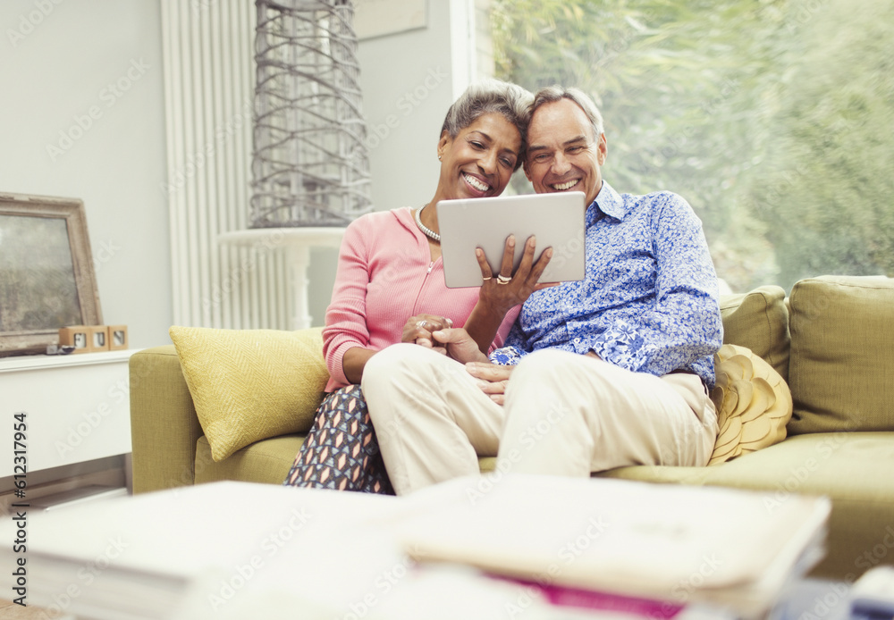 Smiling mature couple using digital tablet on living room sofa
