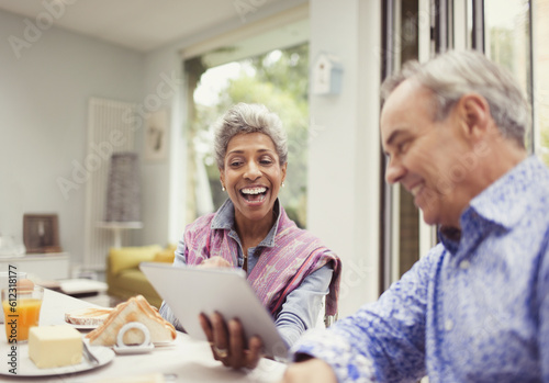 Mature couple laughing and using digital tablet at breakfast table