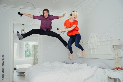 Playful couple jumping on bed listening to music mp3 player headphones