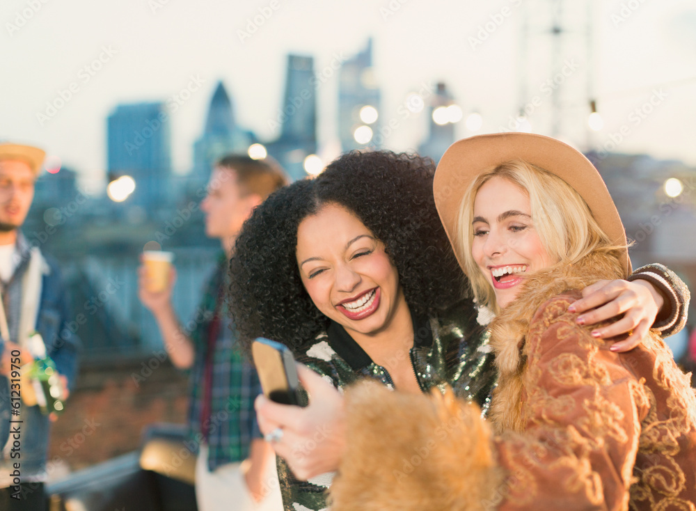 Laughing young women taking selfie at rooftop party Laughing young women taking selfie at rooftop party