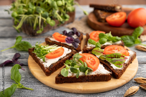 Grain rye bread sandwiches with cream cheese, tomatoes and sunflower microgreen on gray. side view, selective focus.