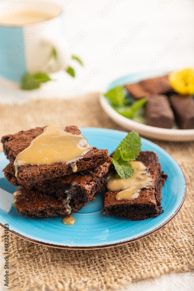 Chocolate brownie with caramel sauce with a cup of coffee on gray concrete, side view, selective focus. Chocolate brownie with caramel sauce with a cup of coffee on gray concrete, side view, selective focus.