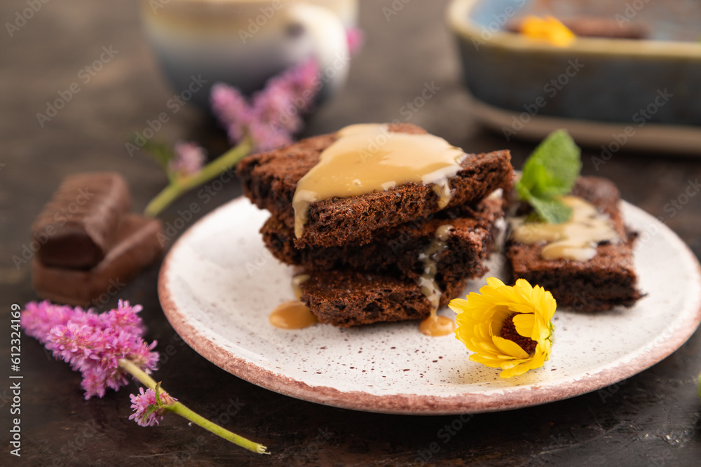 Chocolate brownie with caramel sauce with a cup of coffee on black concrete, side view, selective focus. Chocolate brownie with caramel sauce with a cup of coffee on black concrete, side view, selective focus.