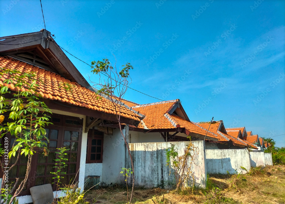One of the houses in Indonesia near the road in a village. White house under the tropical blue sky on a sunny day. White house with traditional clay made tile roof. Close-up.
