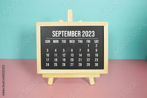 September 2023 monthly calendar on easel stand on pink and blue background