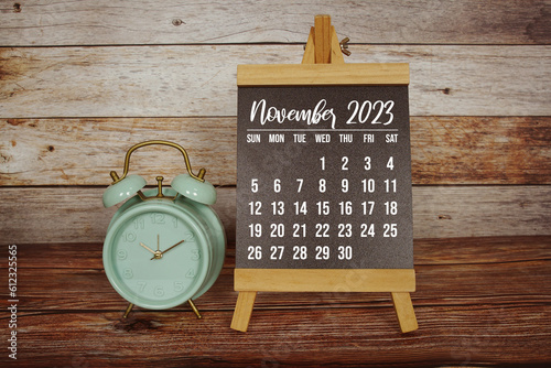 November 2023 monthly calendar and alarm clock on wooden background