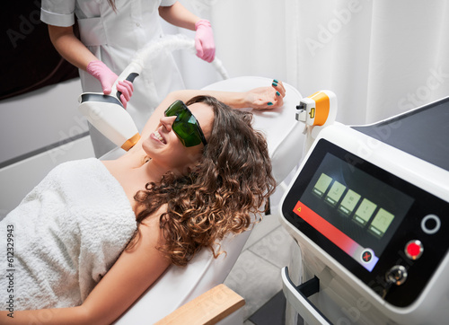 Joyful curly woman with glasses, who is in session of laser hair removal in axillary area of body. Modern, pleasant and painless method of losing unwanted hair.