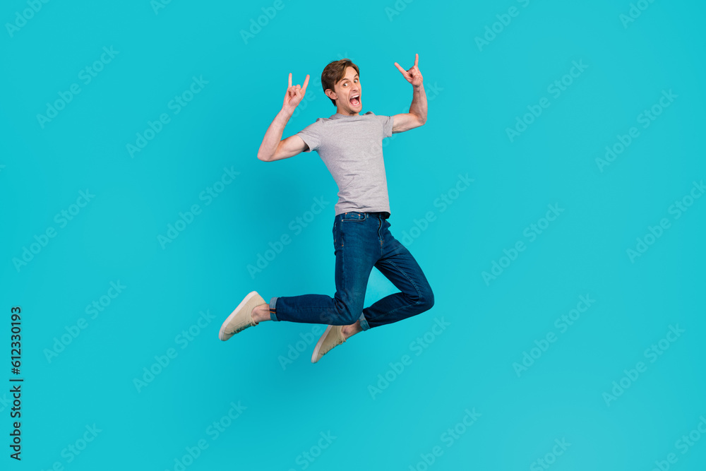 Full length photo of cheerful positive rock fan showing you horned fingers signs jumping up isolated over blue color background