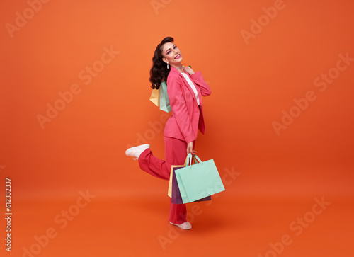 Full-length of happy smiling Fashionable woman carrying shopping bags walking shopping promotion summer sale isolated on orange background.