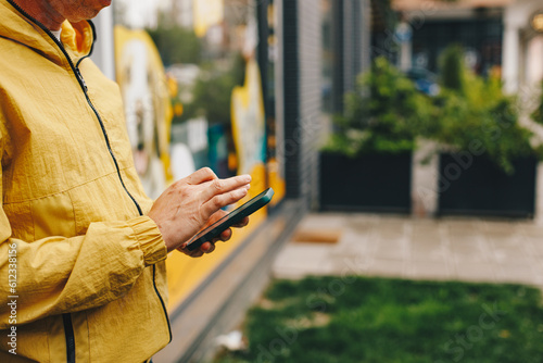 Man in yellow raincoat standing on the street with mobile phone and wireless earphones photo