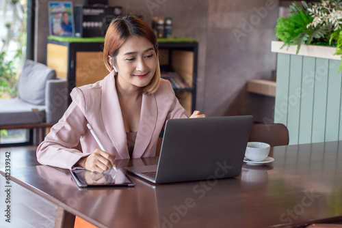Asian businesswoman using laptop and wearing headset talking meeting teamwork to colleagues about plan in Video call conference using tablet writing report,Concept freelance business lifestyle.