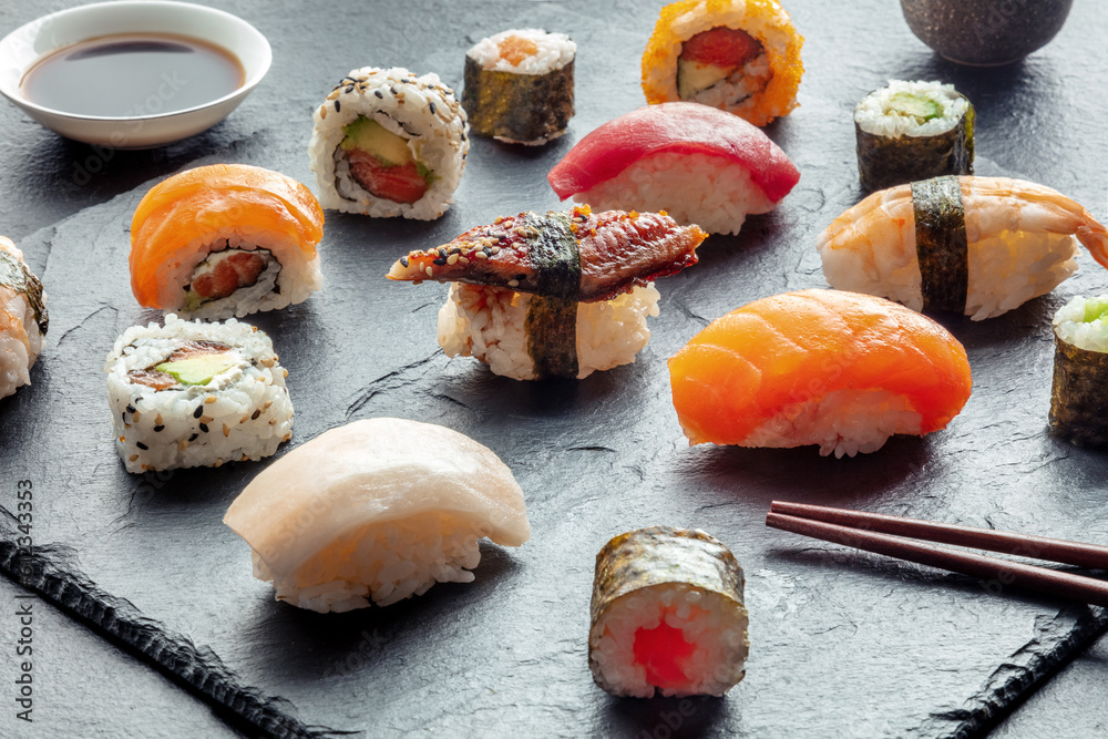 Sushi with chopsticks. Rolls, maki, nigiri on a black background, Japanese food. Salmon, tuna, eel, shrimp and other seafood with rice on a plate at an Asian restaurant Sushi with chopsticks. Rolls, maki, nigiri on a black background, Japanese food. Salmon, tuna, eel, shrimp and other seafood with rice on a plate at an Asian restaurant
