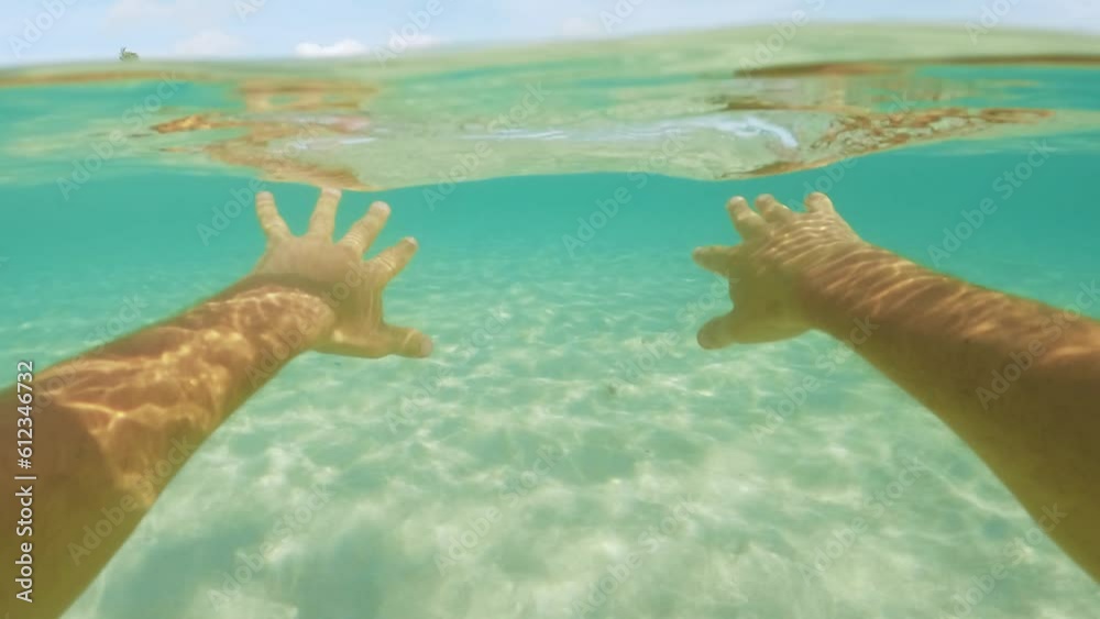 Slow motion POV of men's hands swim in turquoise clear half underwater on a tropical beach with palm trees. Beautiful vacation on the Caribbean sea