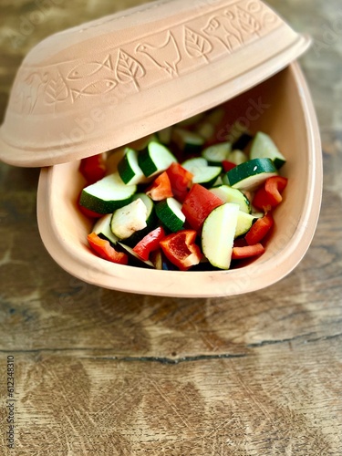 A classic roman pot full of zucchini, aubergine and paprika ready to bake. Healthy ancient cooking style in a clay pot.
